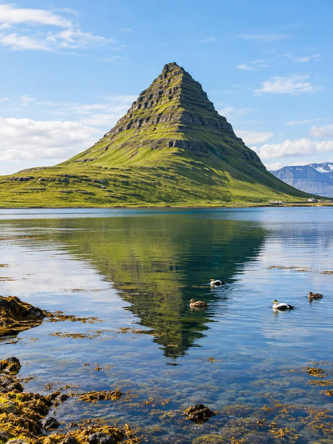 Der Kirkjufell spiegelt sich im stillen Wasser am Ufer des Grundarfjörður-Fjords