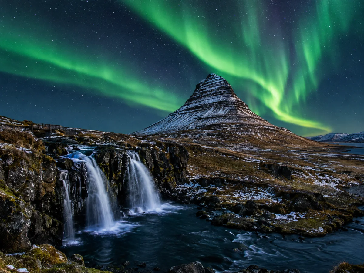 Grüne Nordlichter über dem Kirkjufell und dem Kirkjufellsfoss in einer klaren Nacht mit etwas Schnee