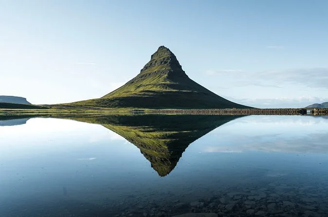 Il Kirkjufell riflesso quasi alla perfezione nell'acqua ferma sotto un cielo pallido