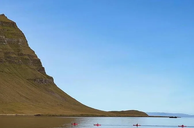 Il ripido pendio del Kirkjufell che riempie la parte sinistra dell'inquadratura, con piccoli kayak sull'acqua calma sotto